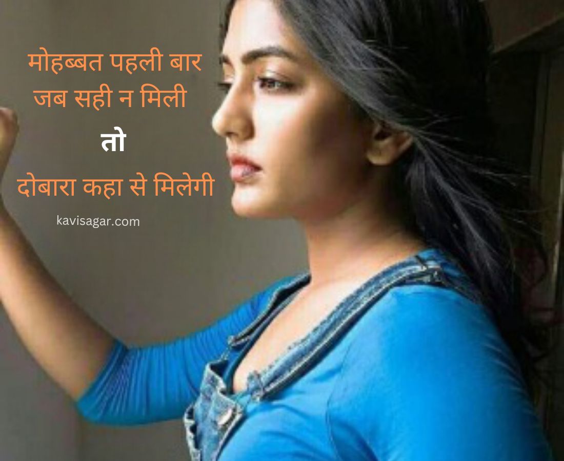 A girl with loose hair in a blue top is thinking with a very broken heart with her hand on the wall.